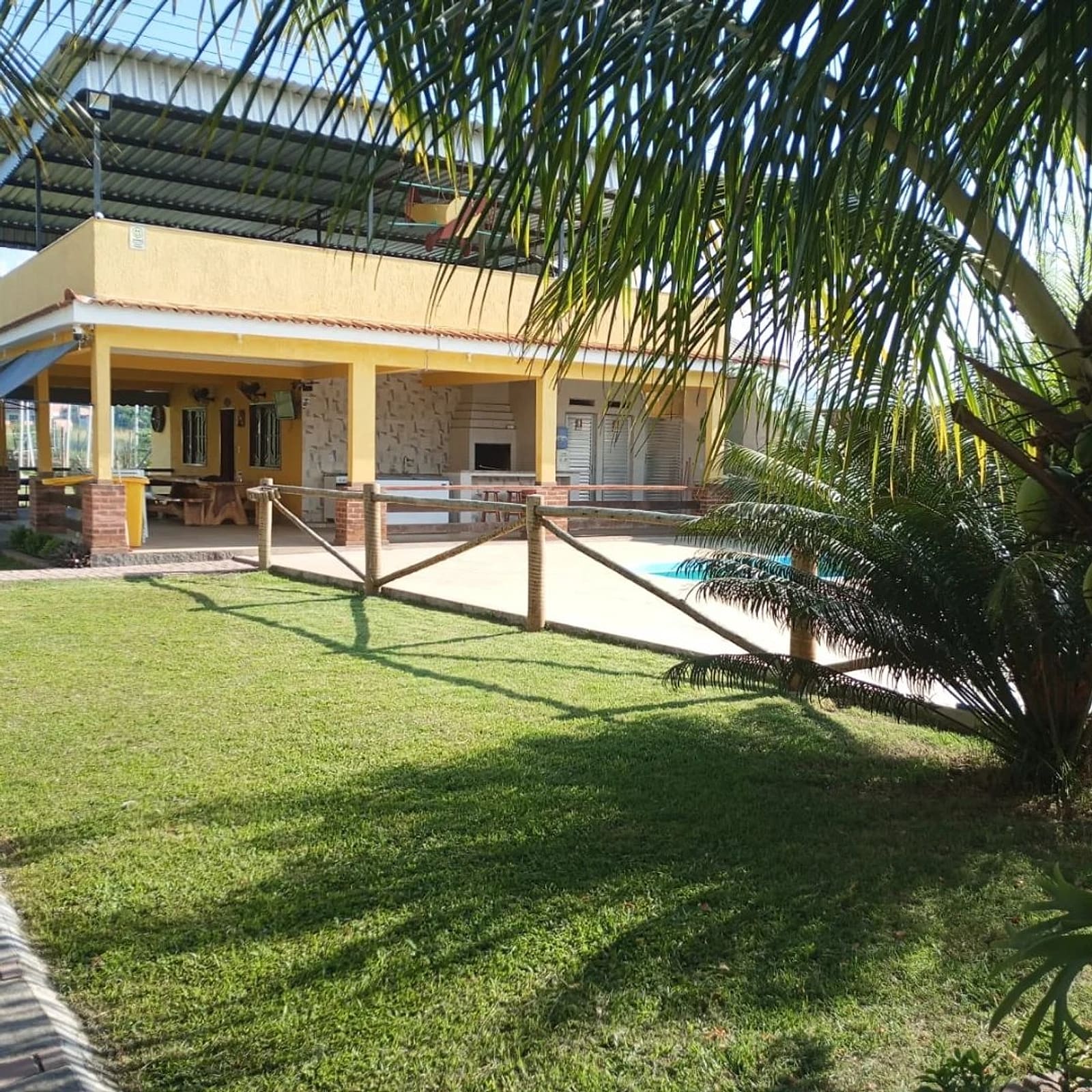 Casa amarela com varanda coberta, vista do gramado, com uma palmeira em primeiro plano