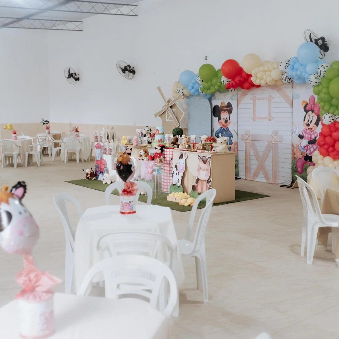 Salão decorado para festa infantil, com mesas e cadeiras brancas